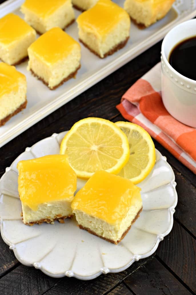 Cheesecake bites topped with lemon curd on a white plate with fresh lemon slices.