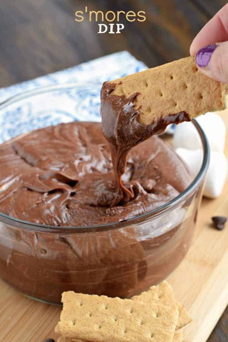 Chocolate smores dip in a glass bowl with a graham cracker being dipped.
