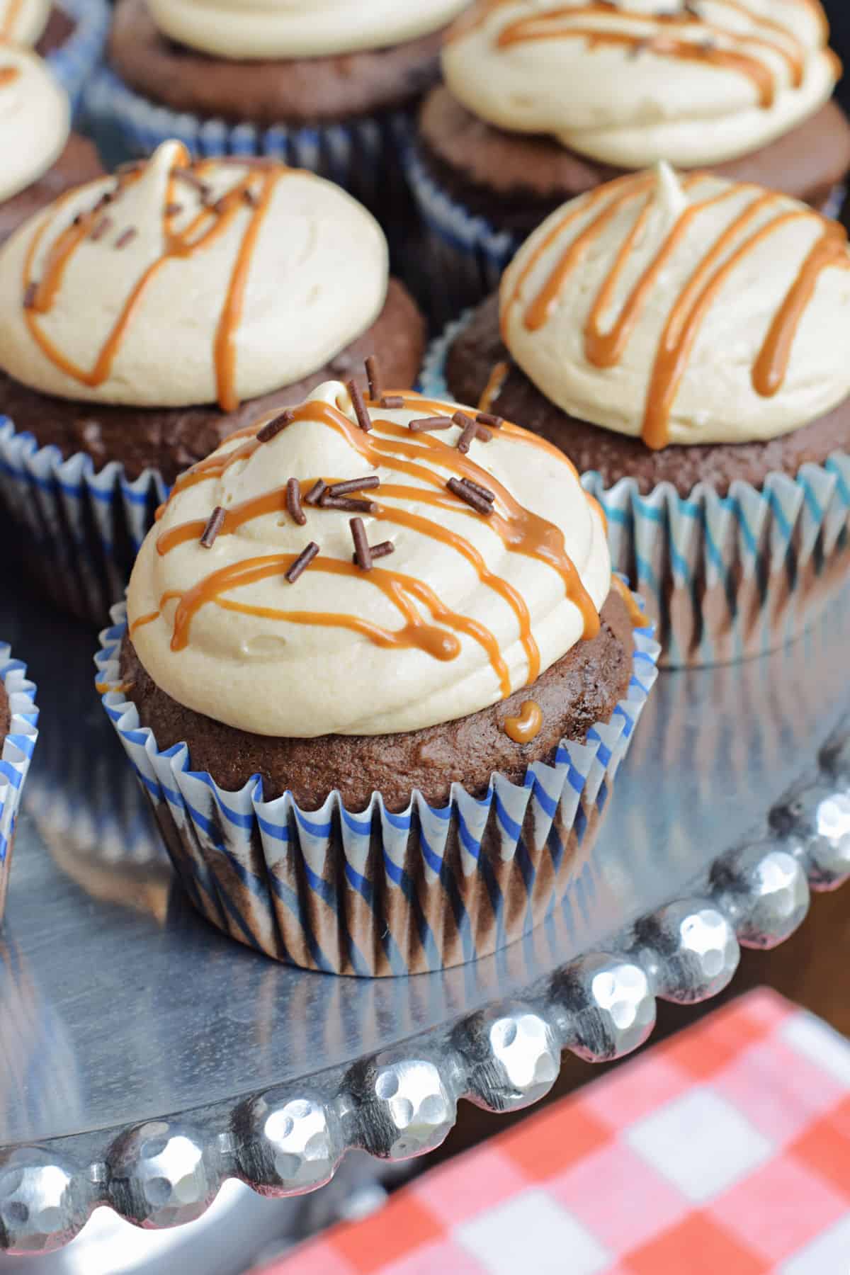 Chocolate cupcakes with biscoff frosting on a metal cake platter.