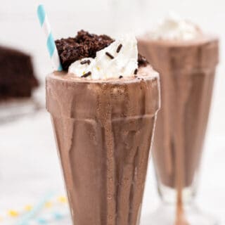 Chocolate cake shake in a sundae glass with whipped cream and a small chunk of chocolate cake.