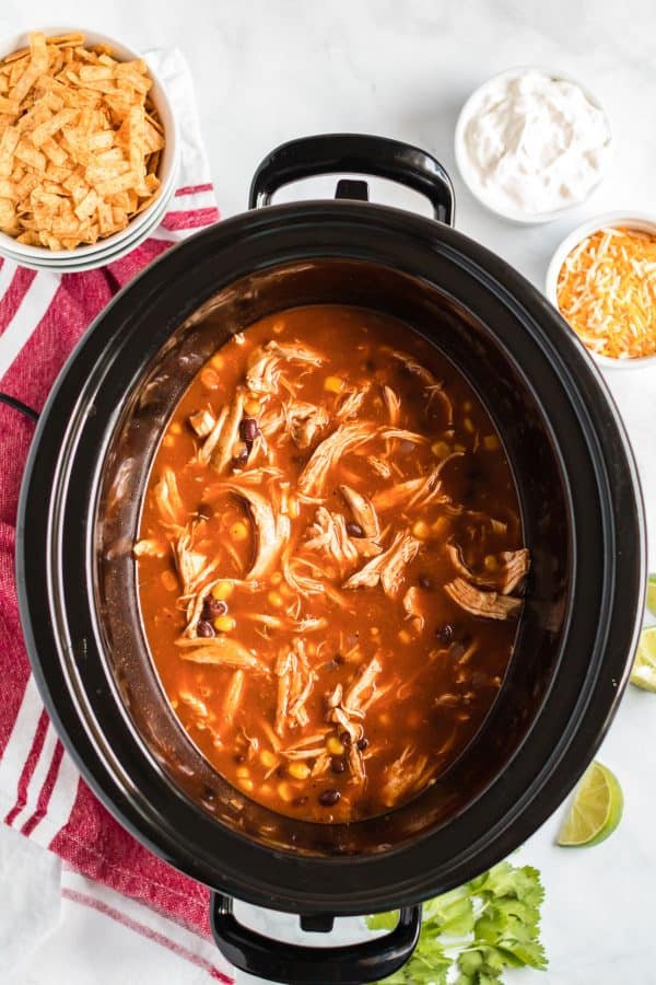 Chicken enchilada soup in a black slow cooker.