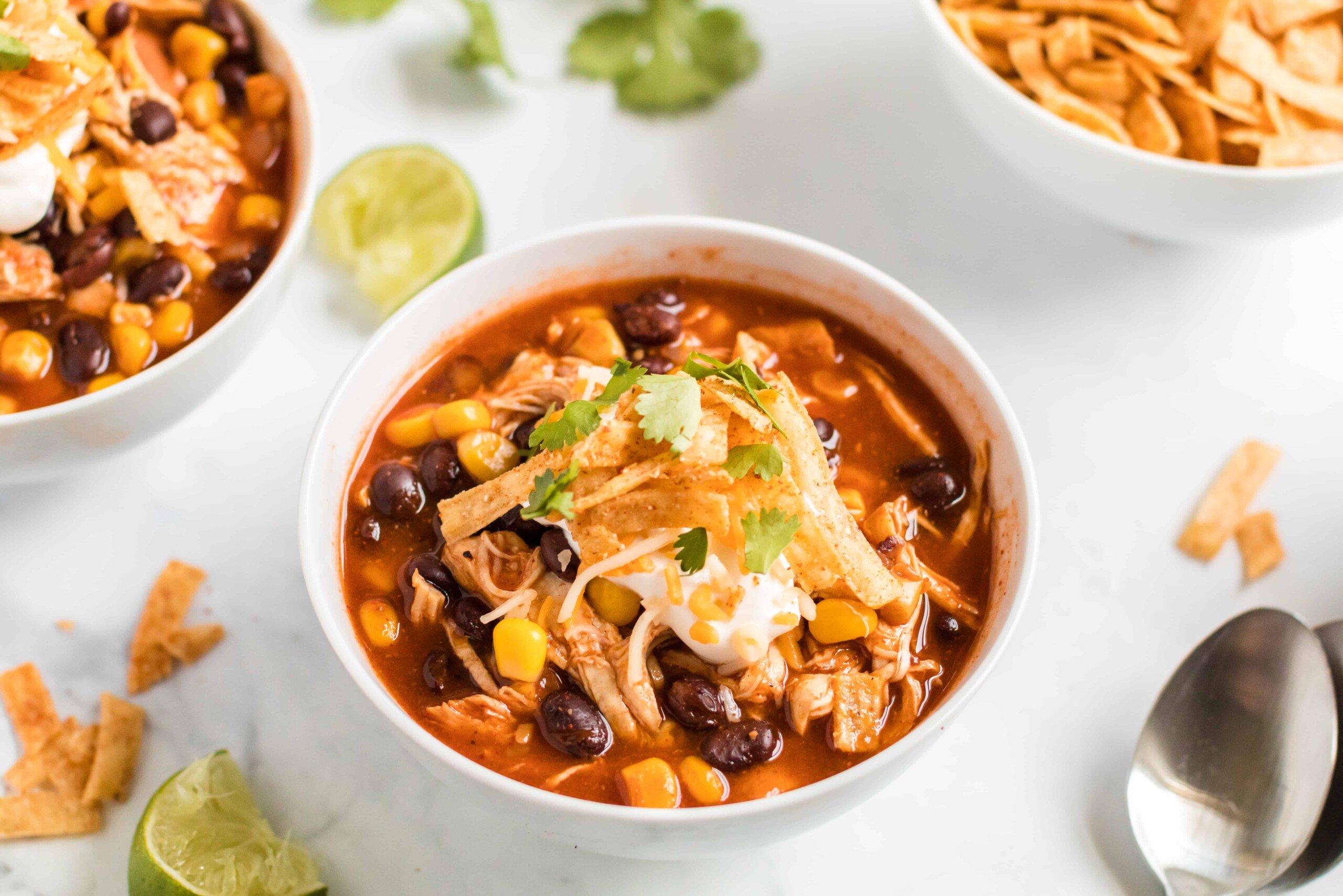 Chicken enchilada soup in a white bowl with tortilla stips and sour cream garnish.
