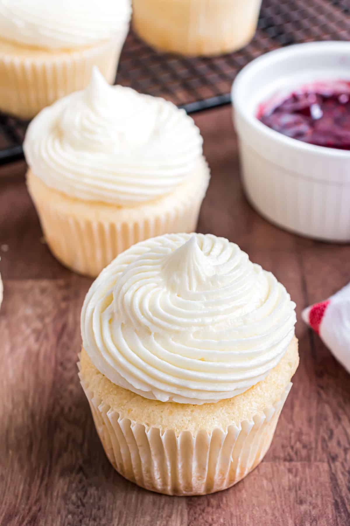 Almond cupcakes with big swirls of frosting. Bowl of raspberry presserves for the filling.