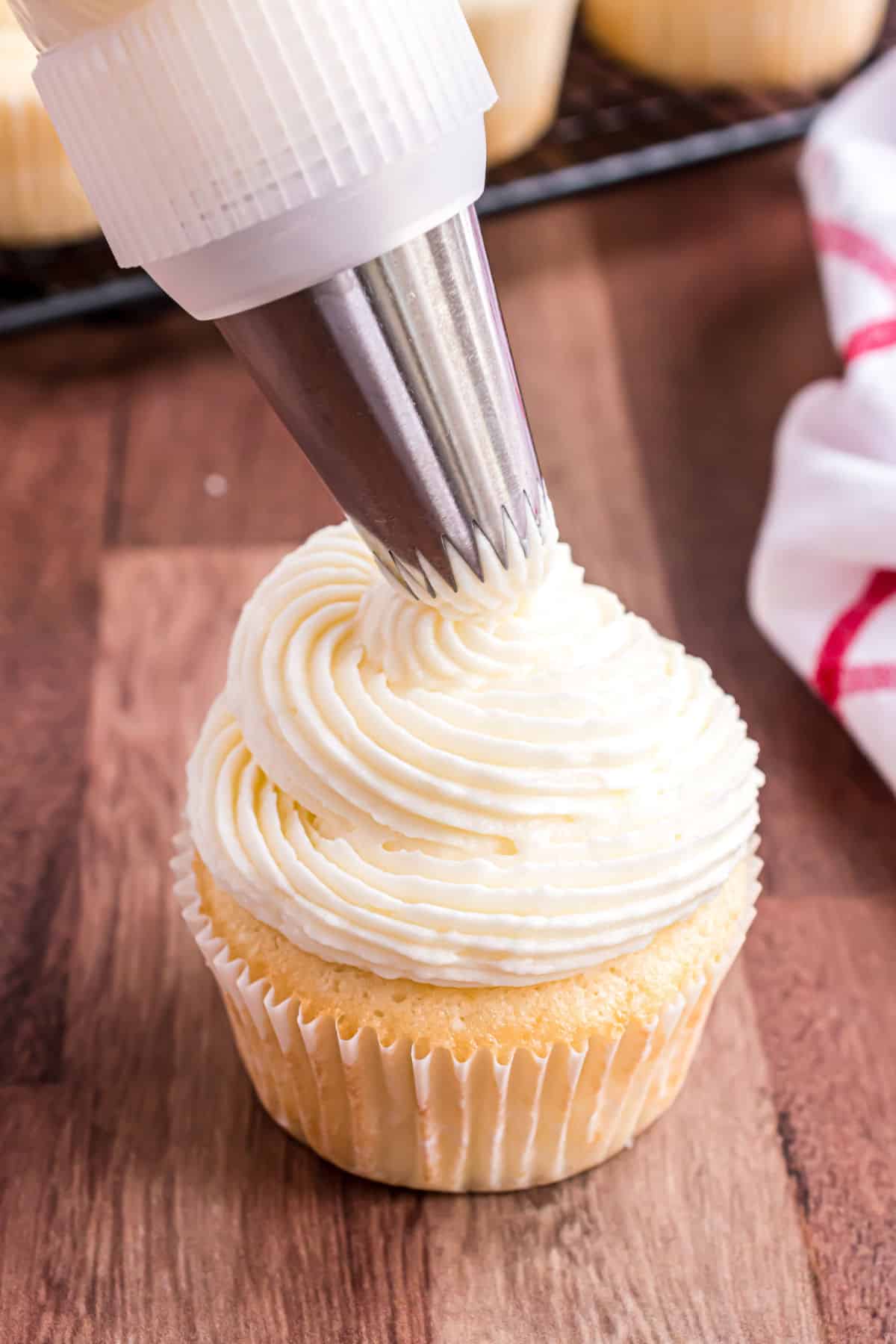 Almond cupcake being frosted with open tip bag.