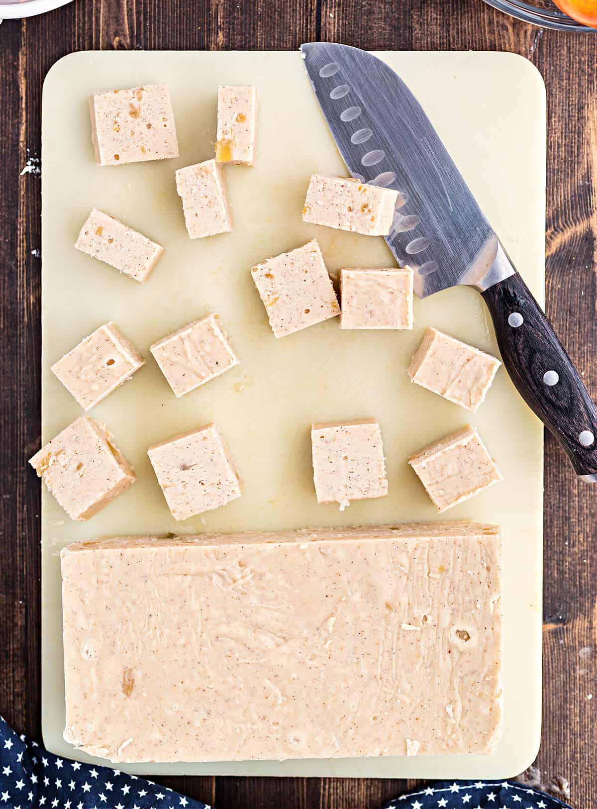 Apple fudge on a cutting board with pieces being cut.