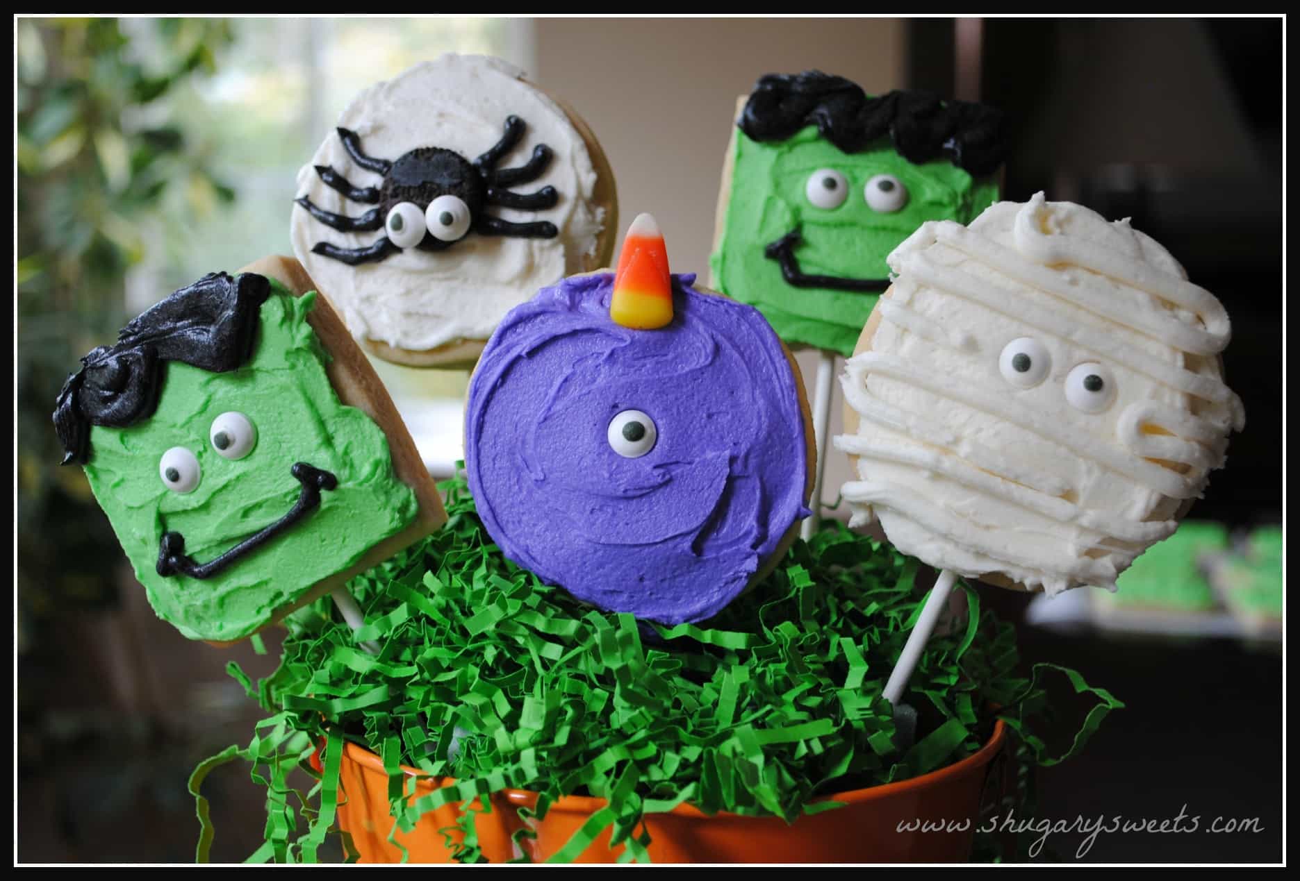 Monster shaped sugar cookies on lollipop sticks in a halloween bucket.