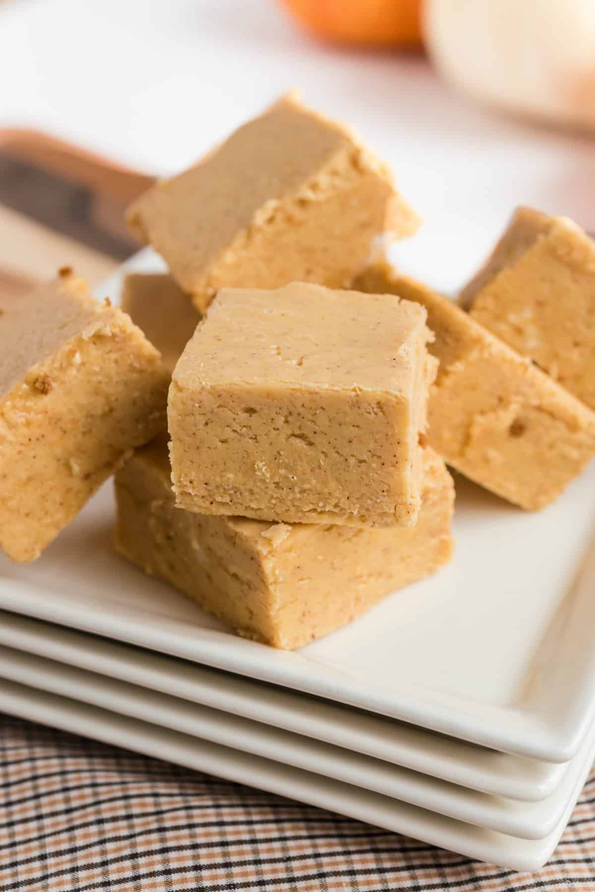 Pumpkin fudge pieces on a stack of white plates.