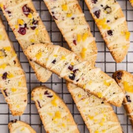 Cranberry orange biscotti topped with white chocolate drizzle on wire rack.