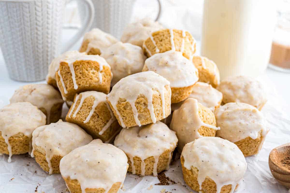 A pile of eggnog muffins with white glaze icing drizzled on top, arranged on parchment paper.