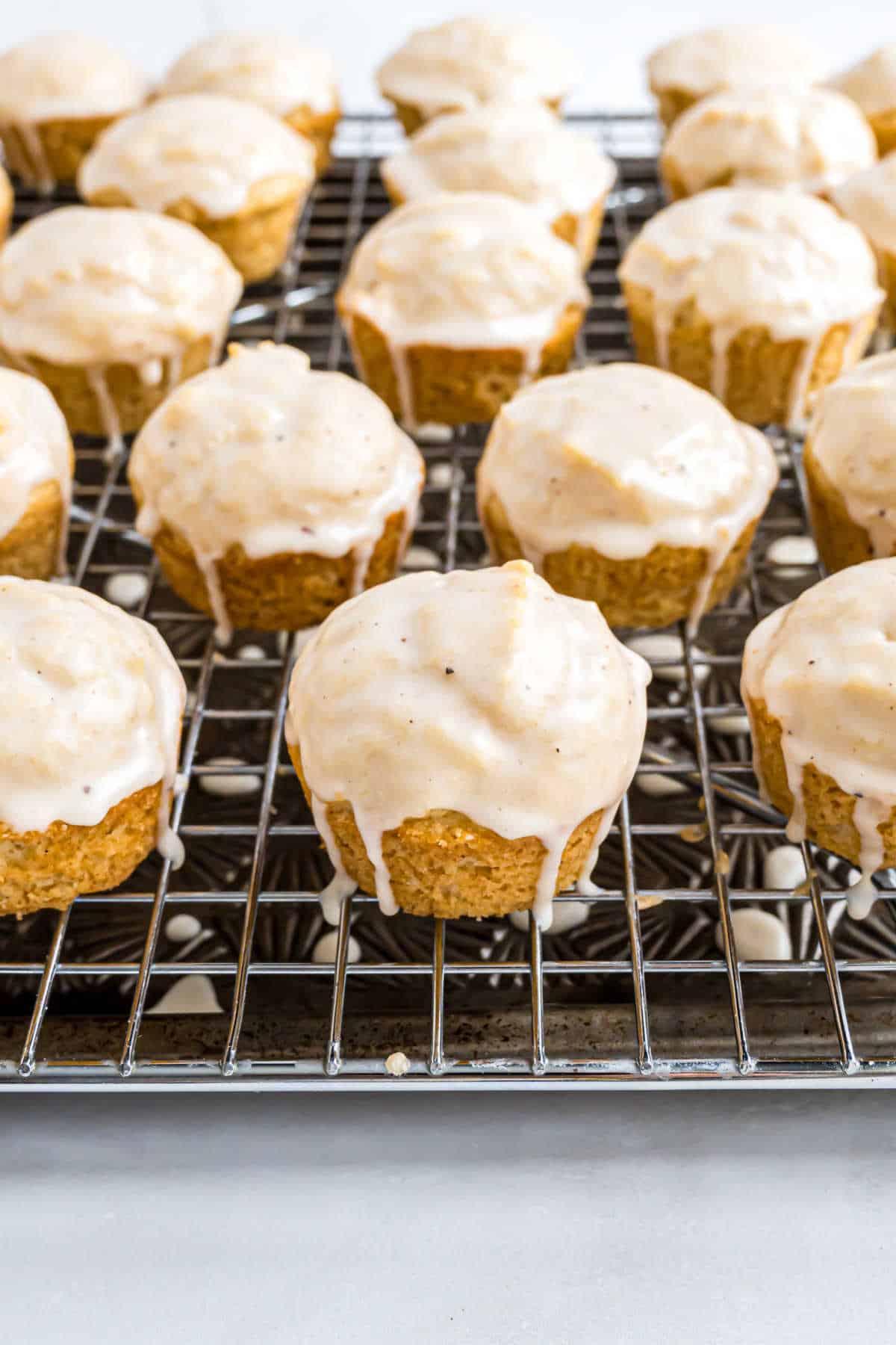 Mini eggnog muffins with vanilla glaze cooling on a wire rack over a baking sheet.