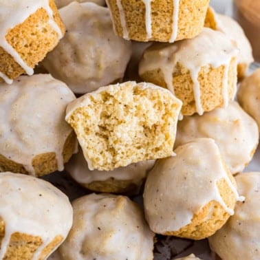 A pile of glazed eggnog muffins, with one muffin cut in half to show the soft, fluffy inside texture.
