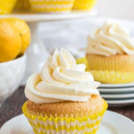 Lemon cupcake topped with lemon frosting on white plate.