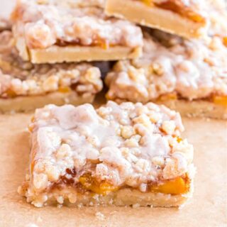 Slice of peach pie bar with glaze on parchment paper.