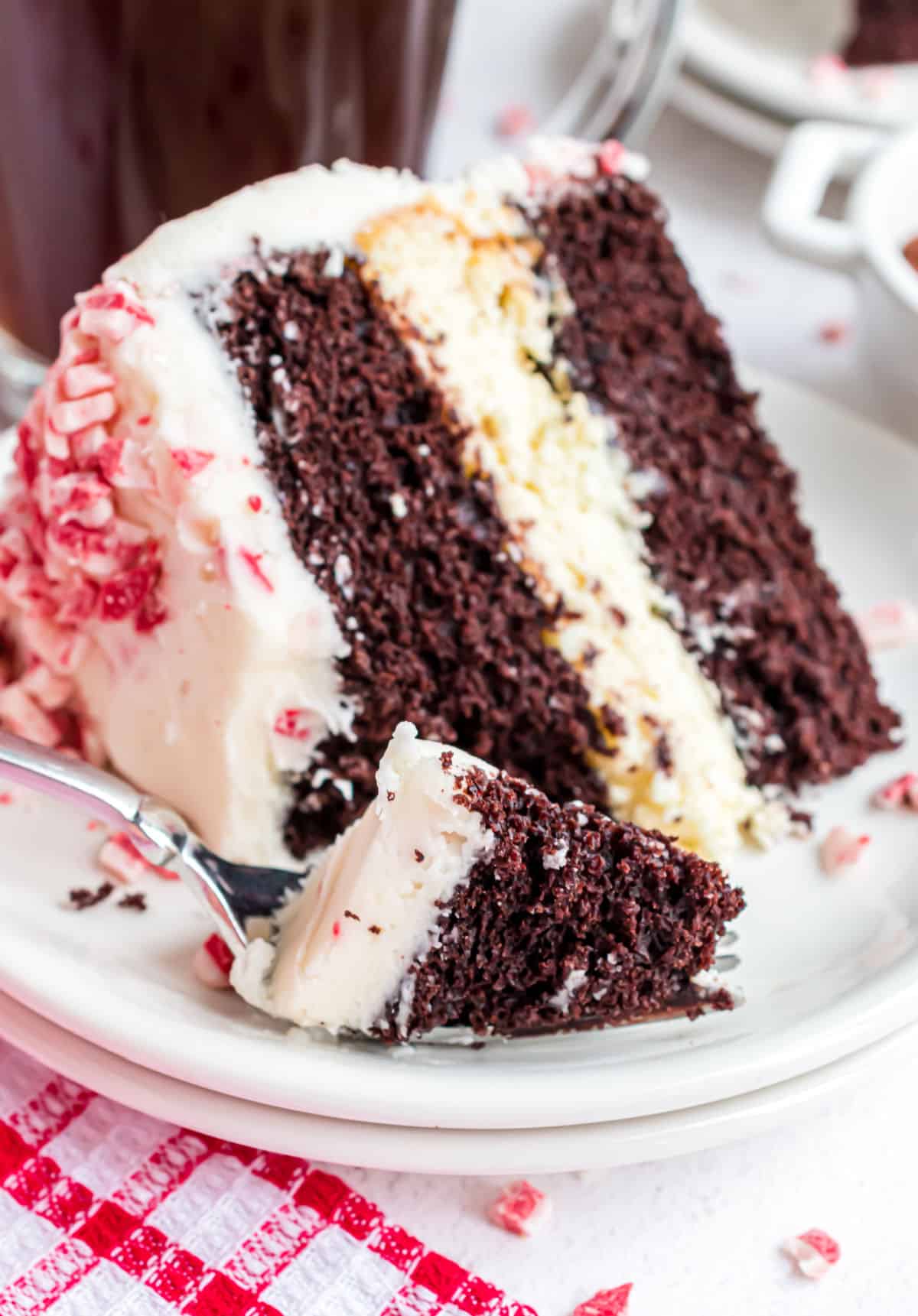 Slice of chocolate peppermint cheesecake cake on a white plate with a fork taking a bite.