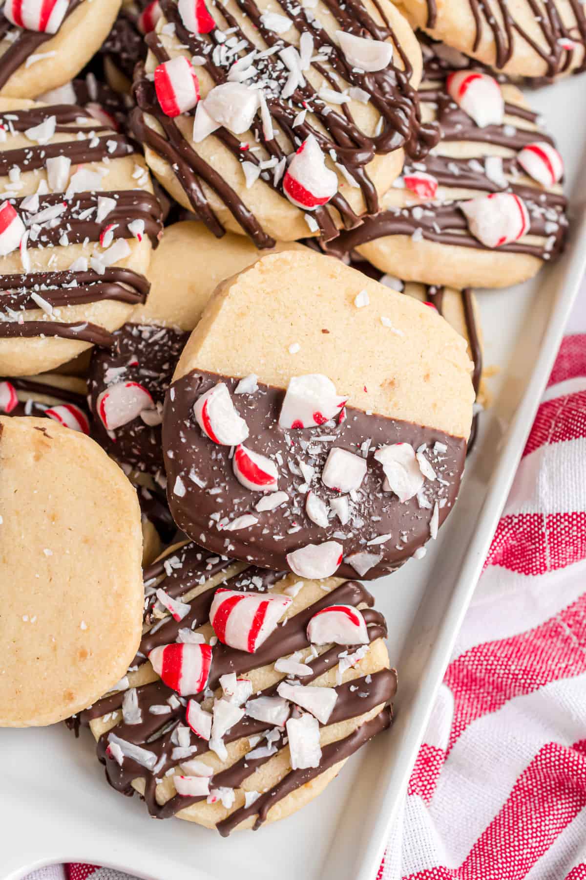 Shortbread cookies dipped in chocolate and sprinkled with crushed candy canes on a white platter.