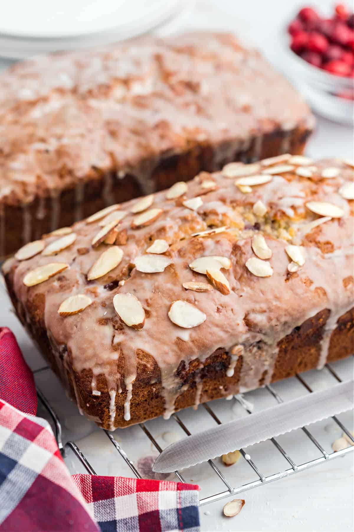 Two loaves of cranberry bread with glaze on a wire cooling rack.