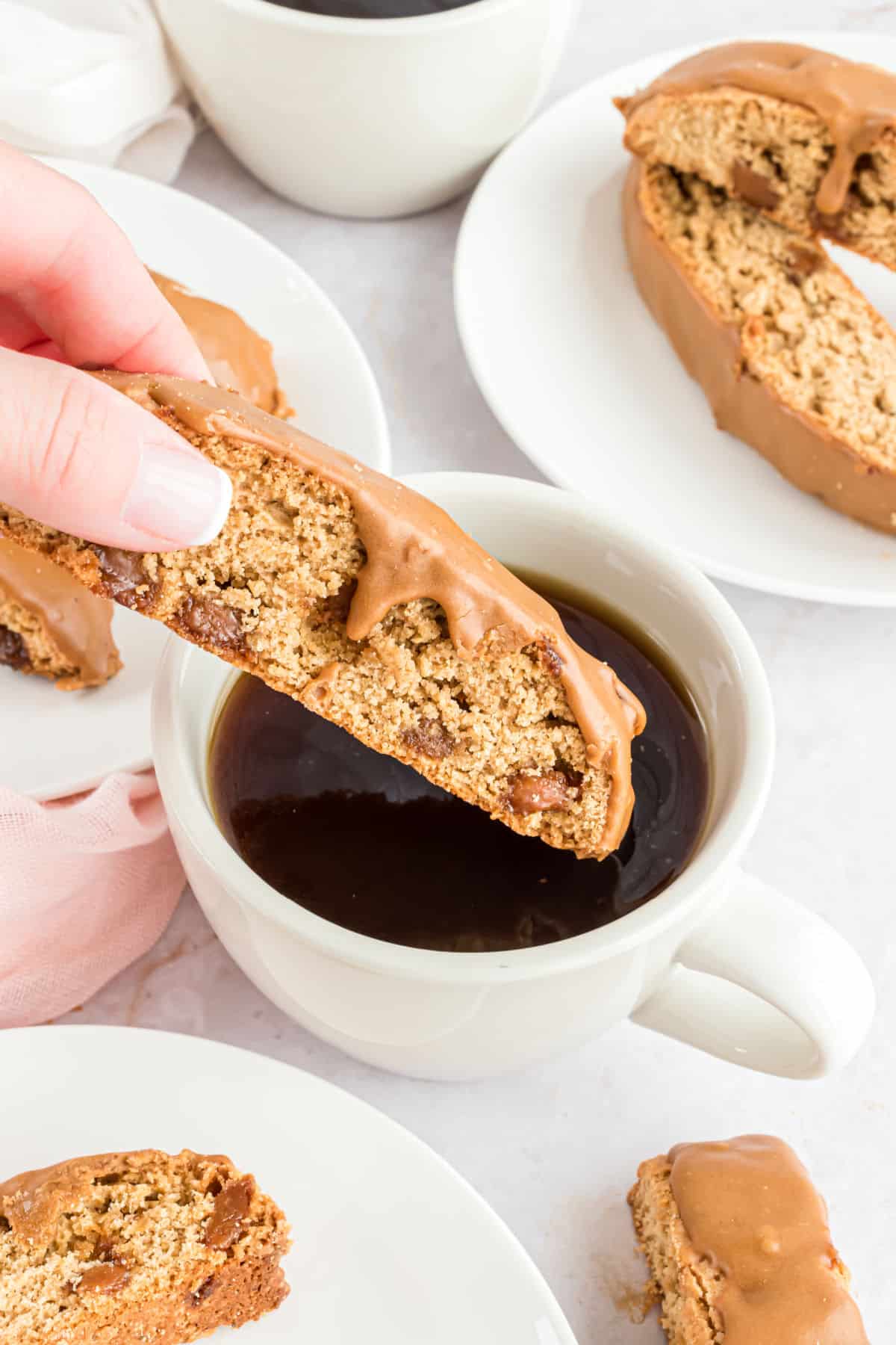 Biscotti being dunked into a small white mug of black coffee.