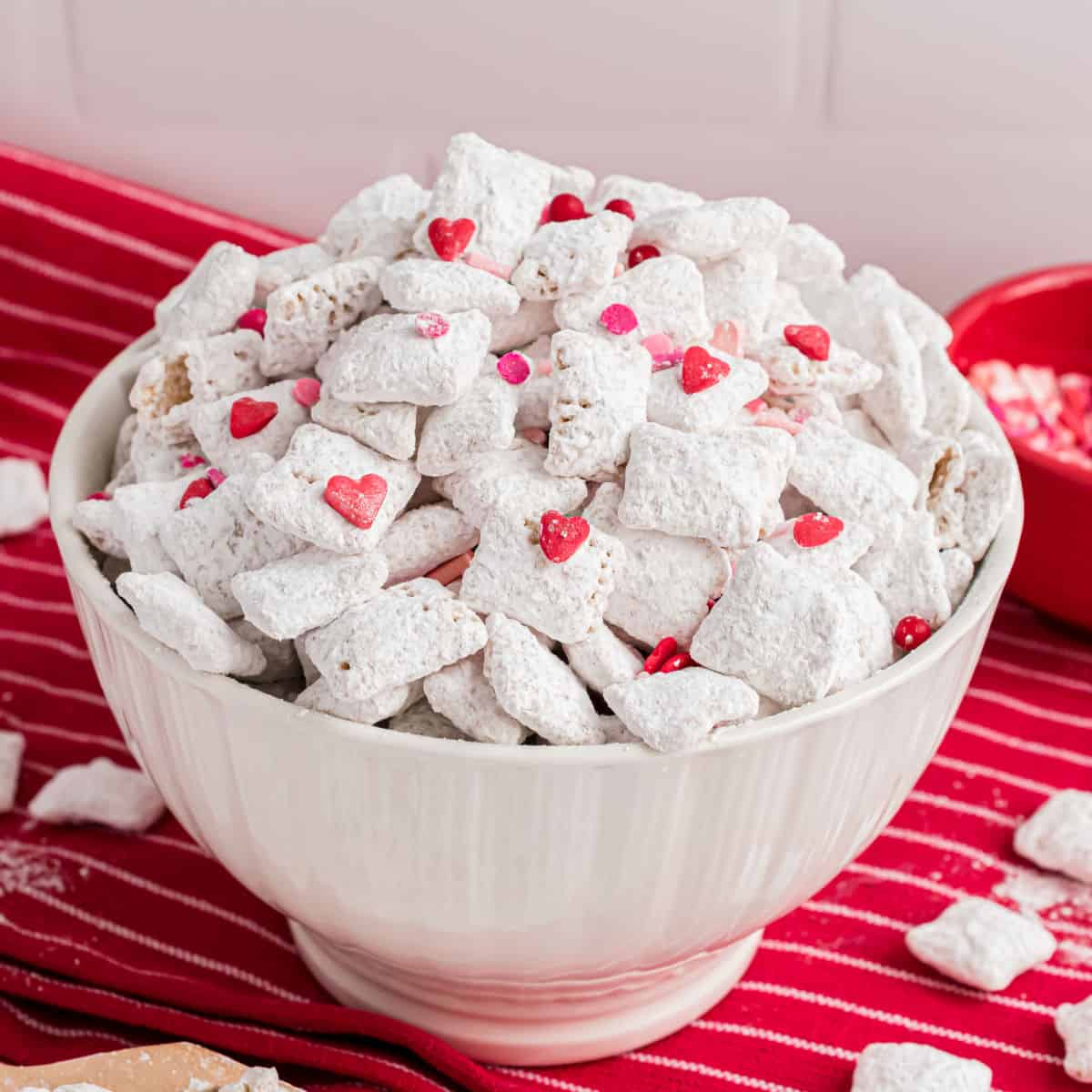 Cherry puppy chow with sprinkles in a white serving bowl.