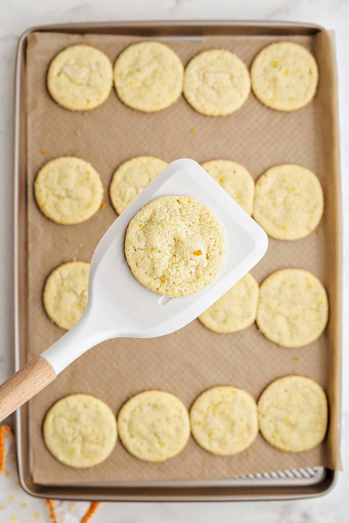 Citrus sugar cookies on cookie sheet being removed with spatula.