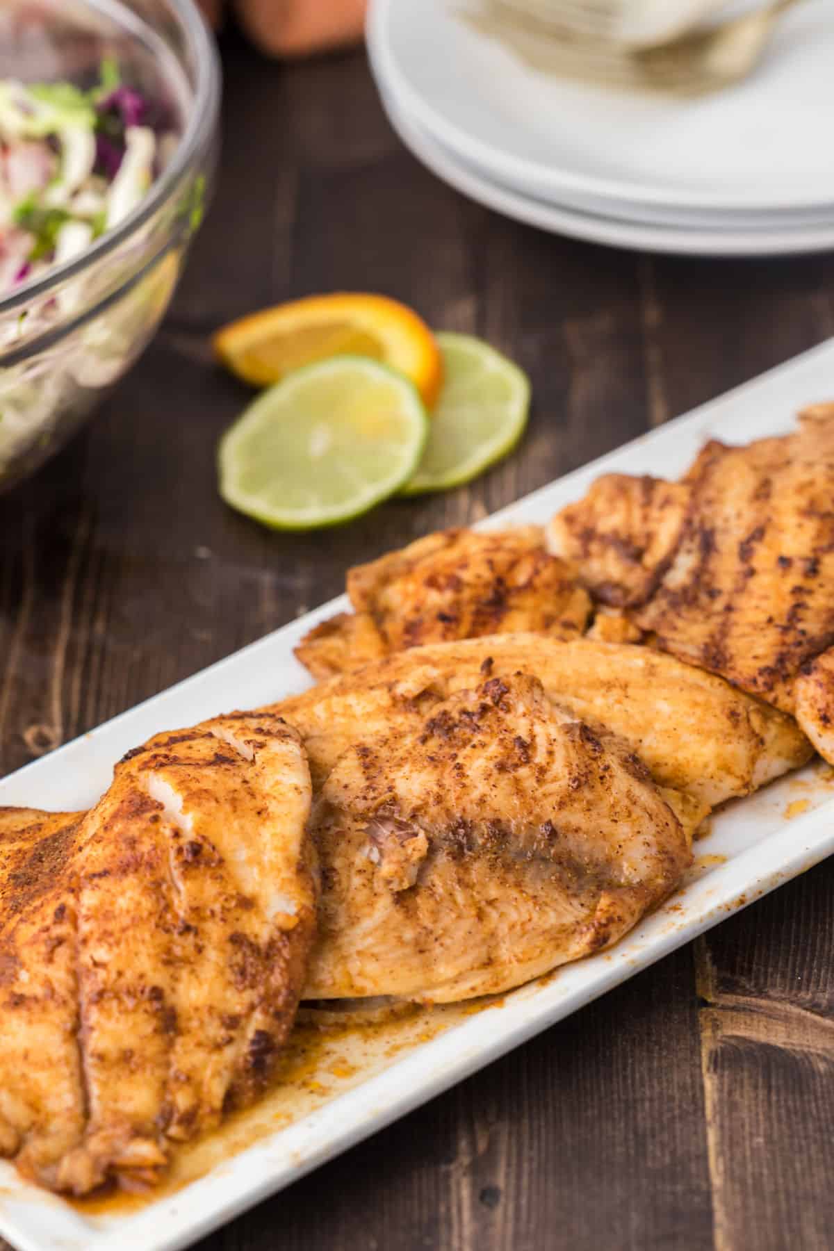 Spicy grilled tilapia on a white rectangular serving plate.