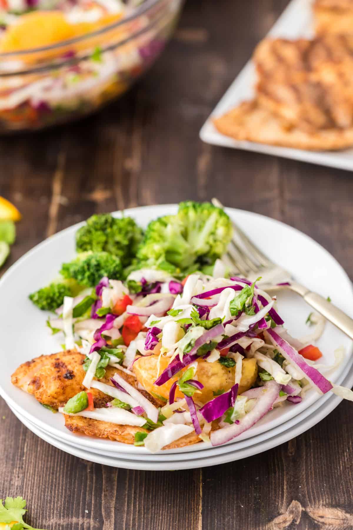 Grilled fish topped with citrus slaw on a white dinner plate.