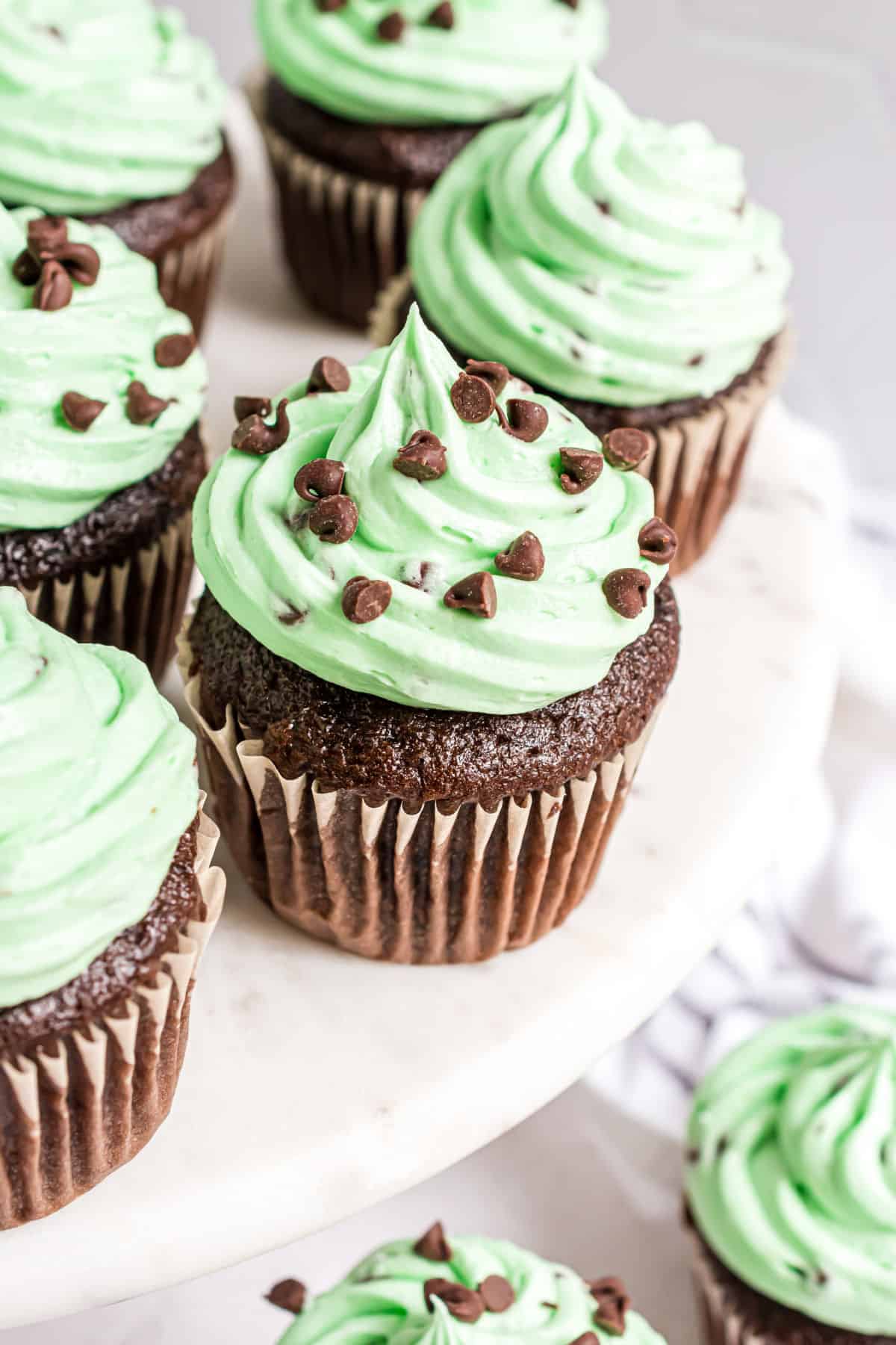White cake platter with mint chocolate chip frosted chocolate cupcakes.