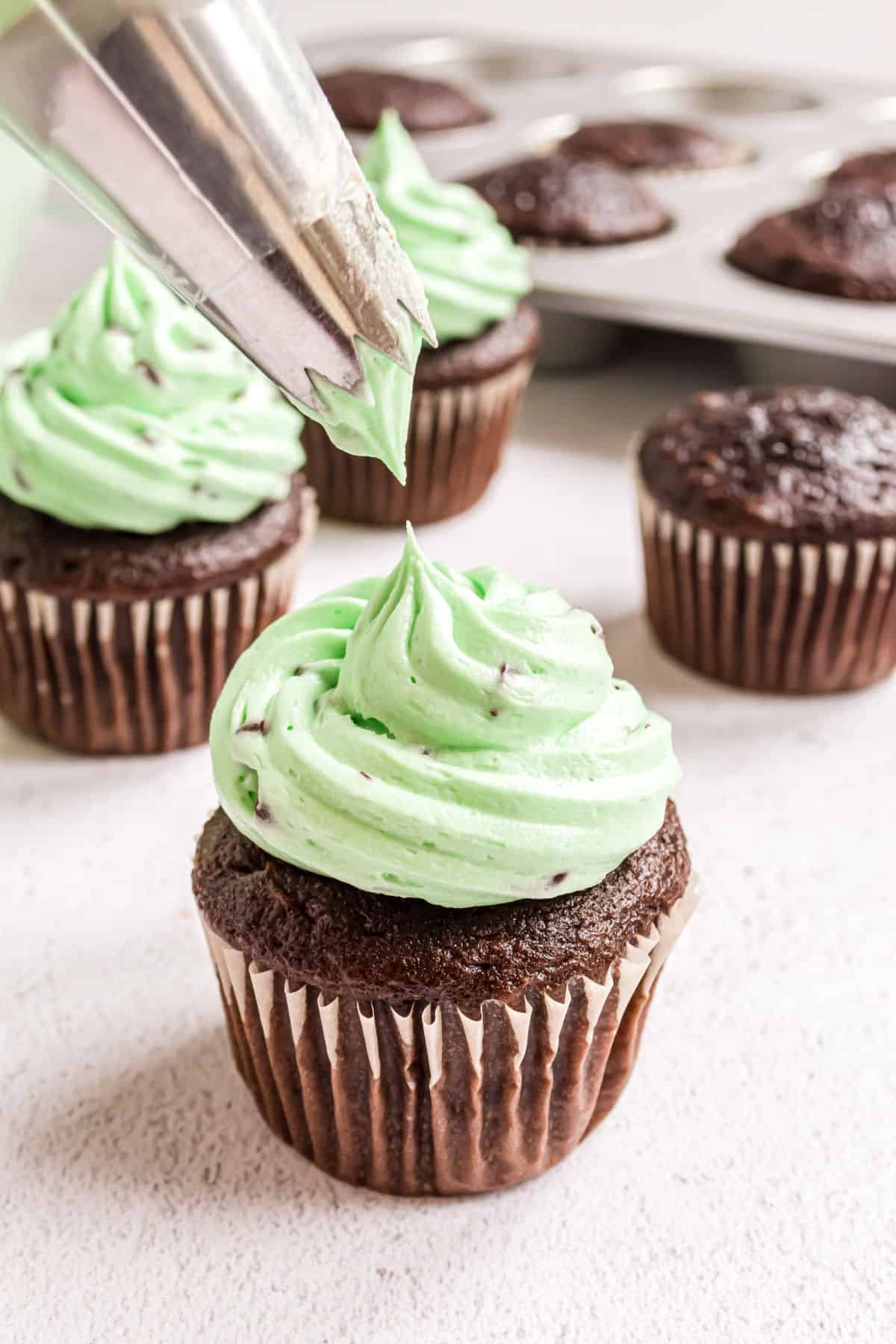 Mint chocolate chip frosting being piped onto a chocolate cupcake.