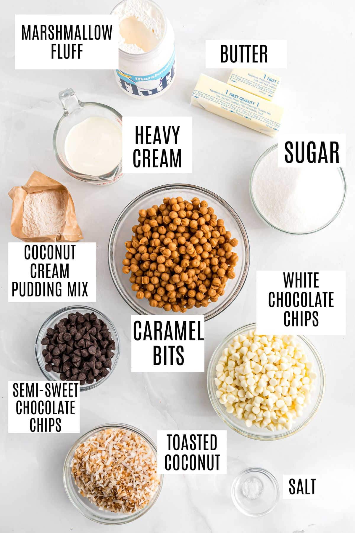 Flat lay of labeled dessert ingredients in bowls, including caramel bits, chocolate chips, coconut, and marshmallow fluff—perfect for making homemade samoa fudge.