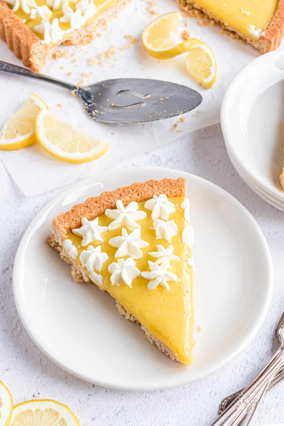 Slice of lemon tart with whipped cream on a white plate.