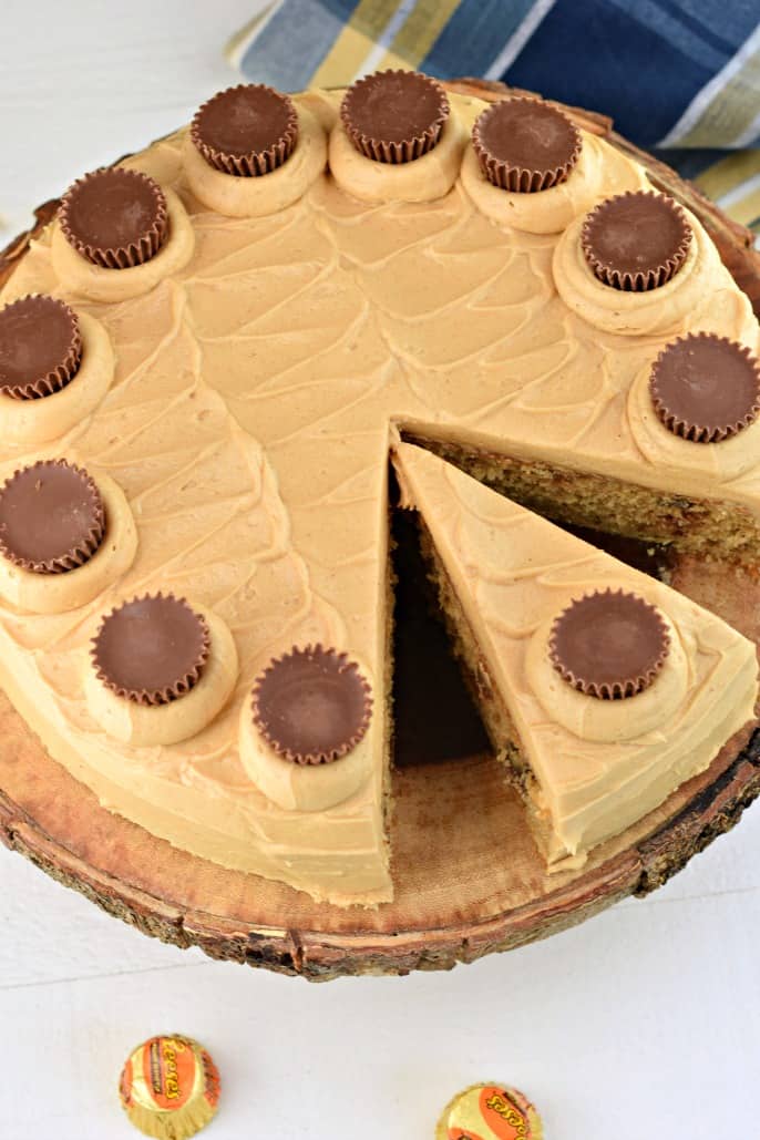 Cake with peanut butter frosting and Reese's peanut butter cups on a wooden cake plate.