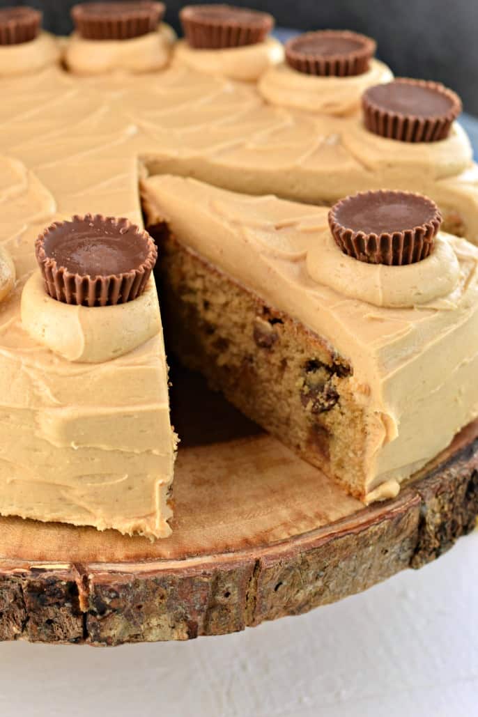 Peanut Butter cake on a wooden cake plate and topped with reese's peanut butter cups.