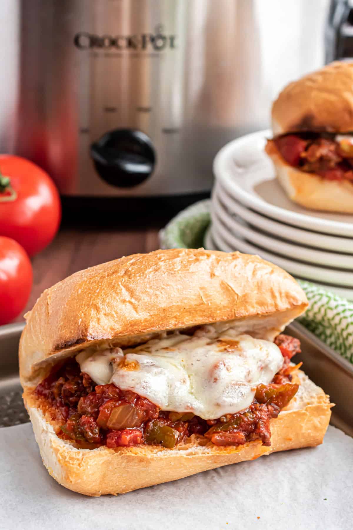 Cheesy sausage and pepper sandwich with crockpot in background.