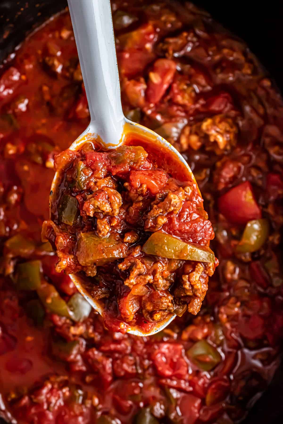 Sausage and peppers being spooned out of crock pot.