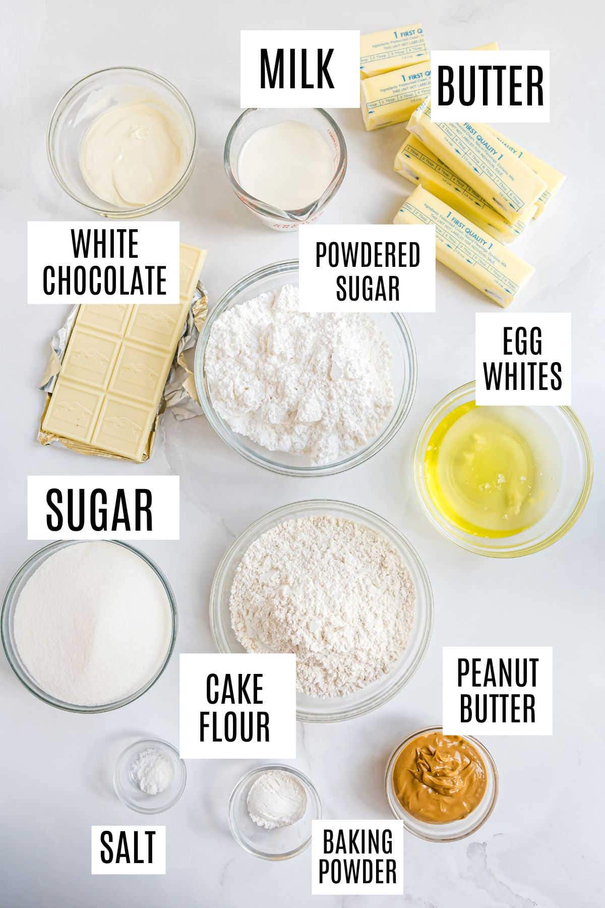 Various baking ingredients in bowls and plates, each labeled: milk, butter, white chocolate, powdered sugar, egg whites, sugar, cake flour, peanut butter, salt, baking powder—perfect for making delicious white chocolate cupcakes.