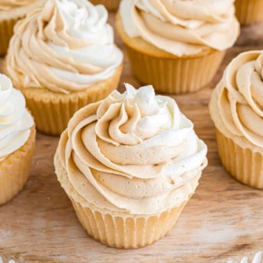 White chocolate cupcakes with swirled tan and white frosting sit beautifully on a wooden surface.