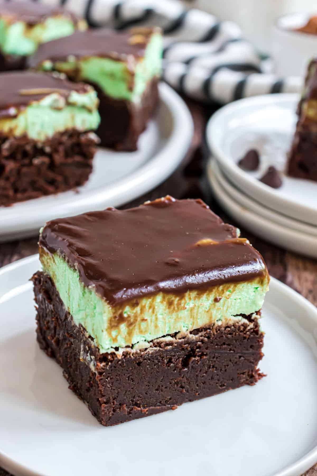 Slice of chocolate brownie on white plate, topped with mint green filling and chocolate ganache.