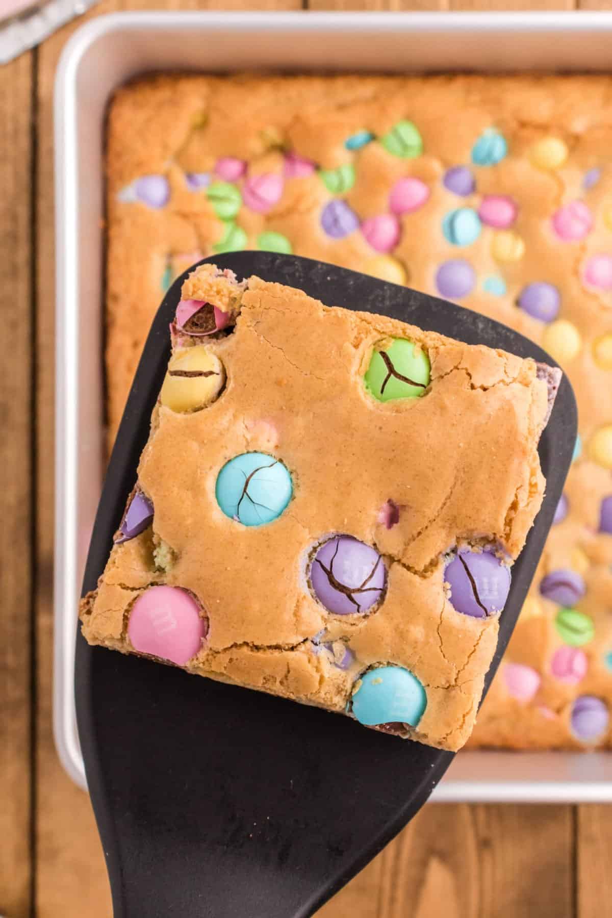 Blondies with pastel M&M's cut into squares, one on a spatula.