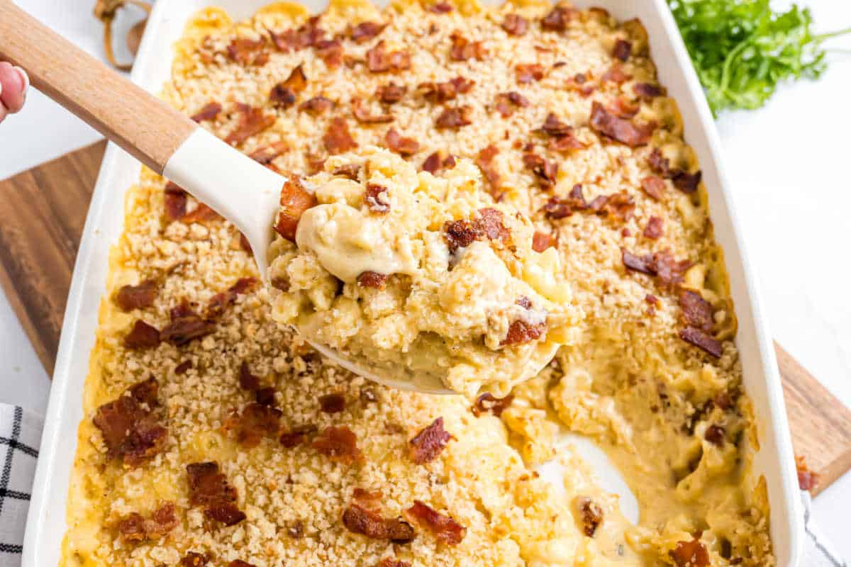 A serving of creamy gouda bacon macaroni and cheese with crispy breadcrumbs is being scooped from a casserole dish.