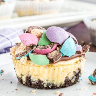 Malt ball cheesecake with chocolate ganache and candy on a white plate.