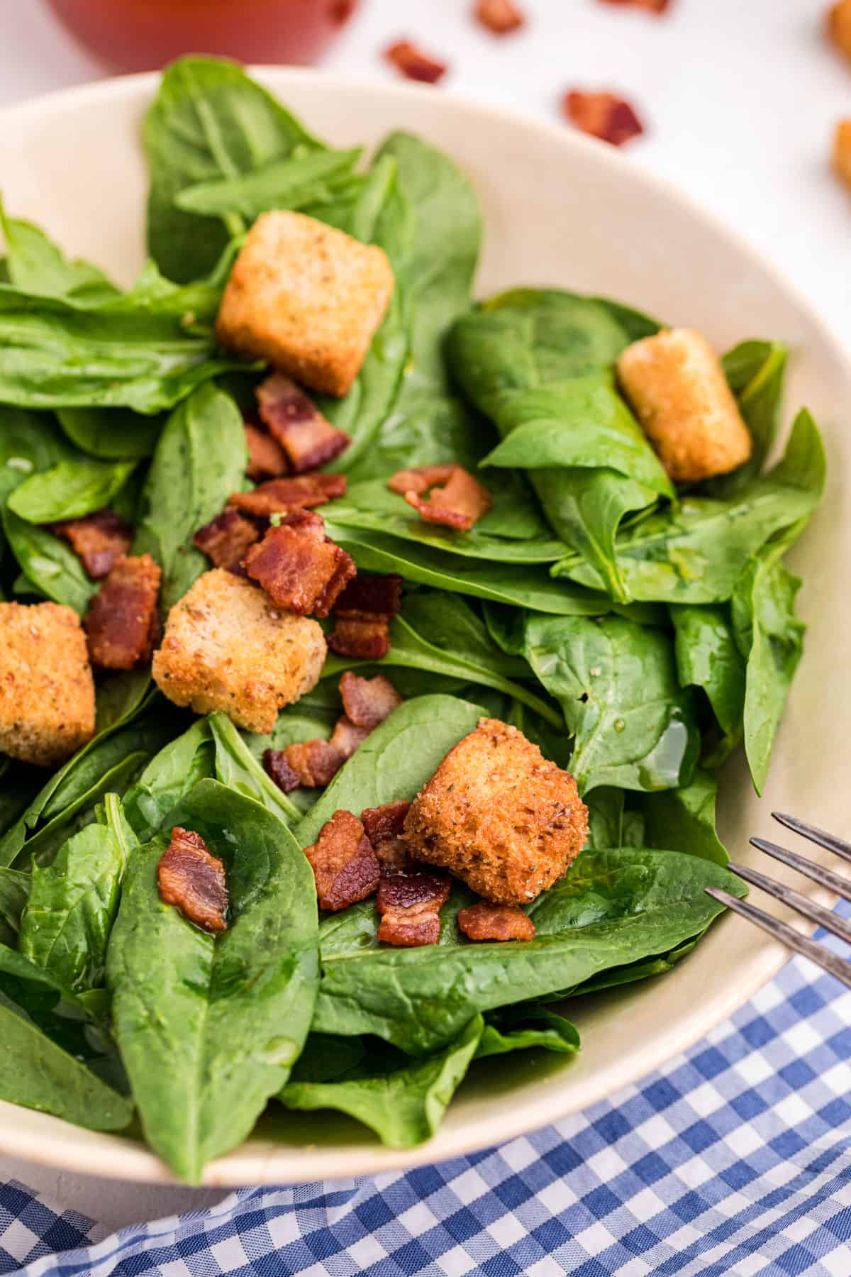 Spinach salad in a white bowl with croutons and bacon.