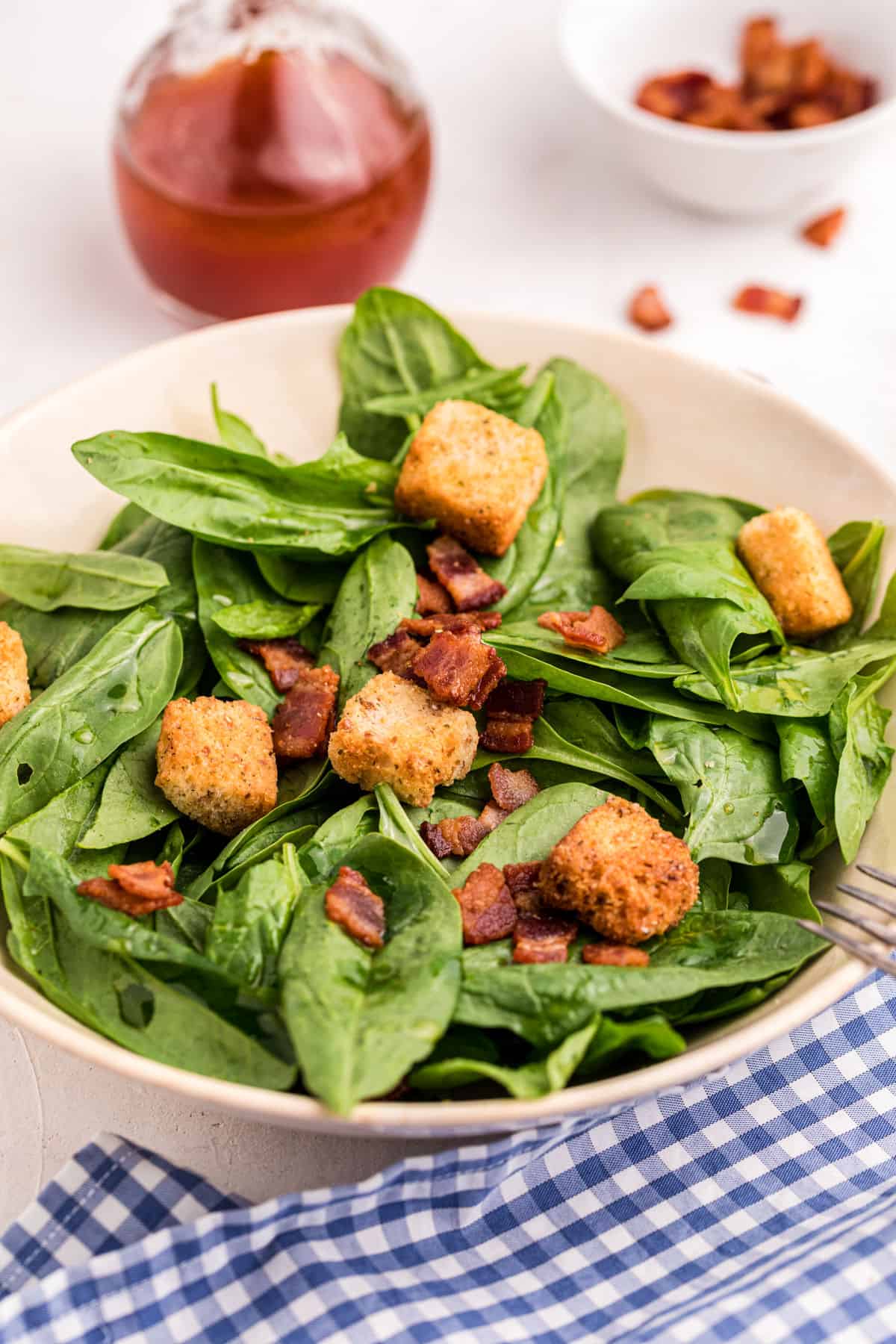 Spinach salad with bacon, croutons, and dressing.