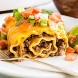 Lasagna roll-up with enchilada beef rollups-style ground beef, melted cheese, and fresh salsa on a white plate with a fork.