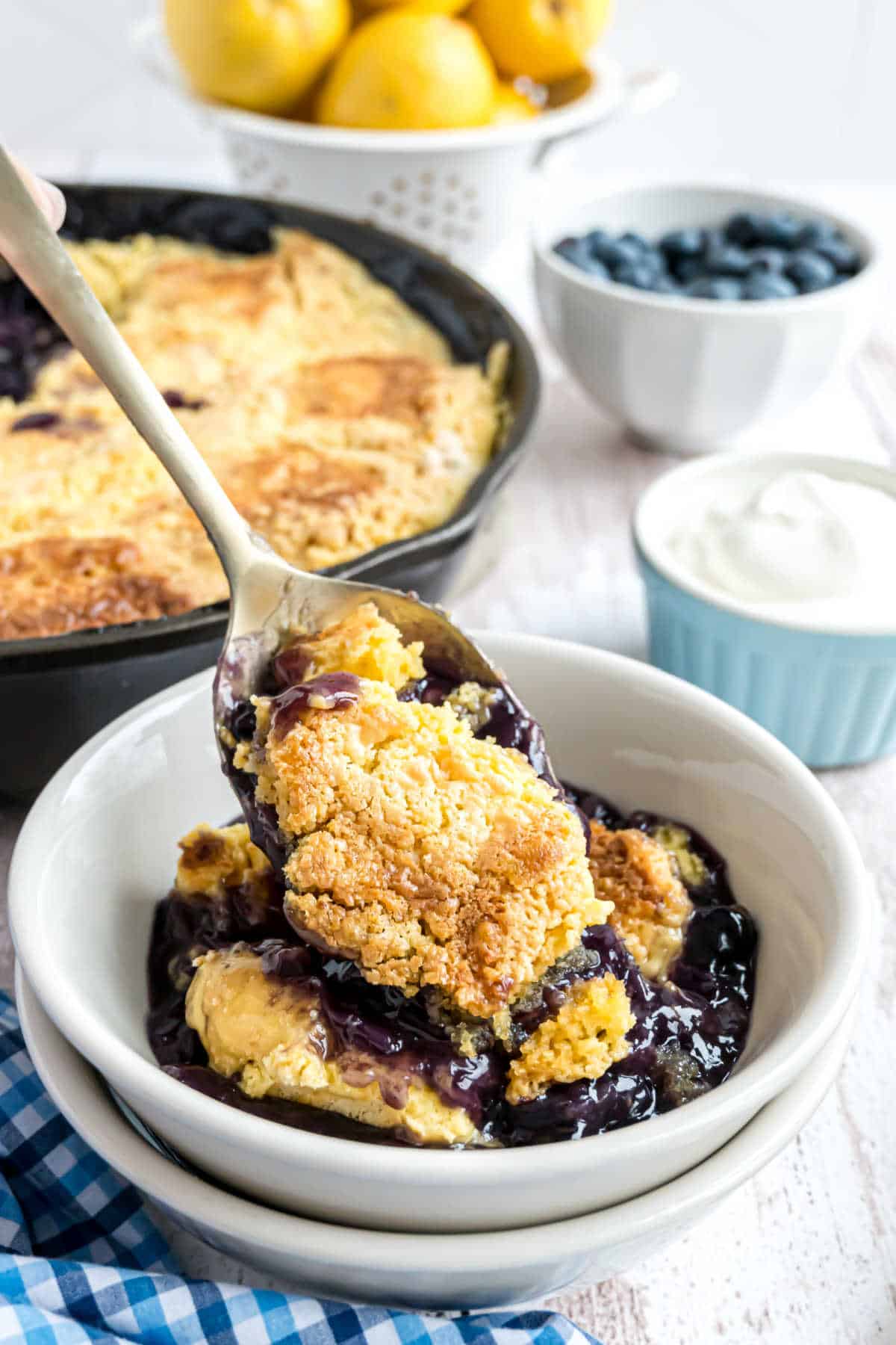 Spoonful of blueberry dump cake being spooned into a stack of white bowls.