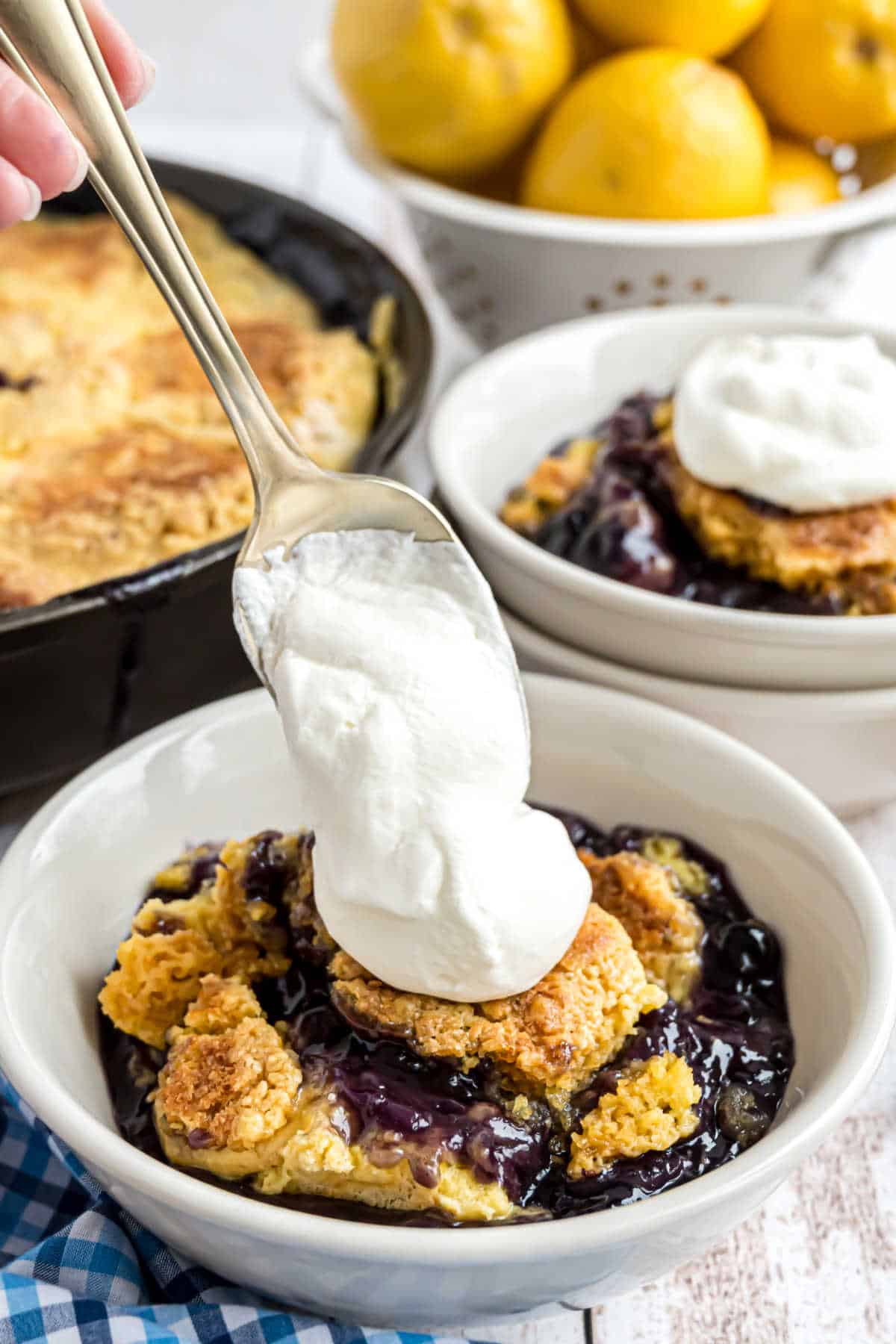 Blueberry cake with a dollop of whipped cream being put on top.
