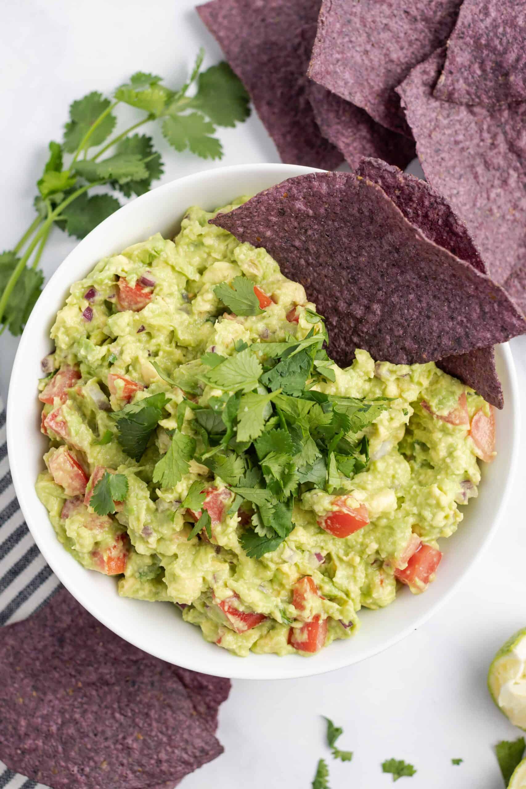 Bowl of chunky guacamole garnished with blue corn chips and cilantro