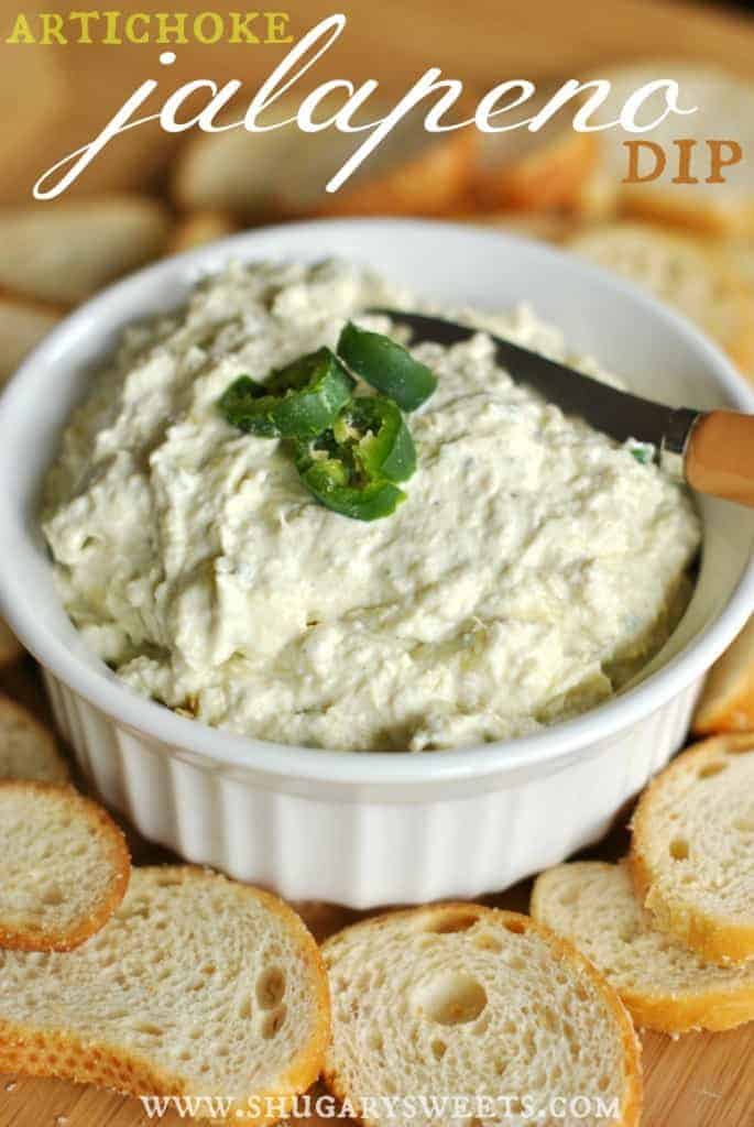White bowl with artichoke dip topped with slices of fresh jalapenos and served with toasted baguette slices.