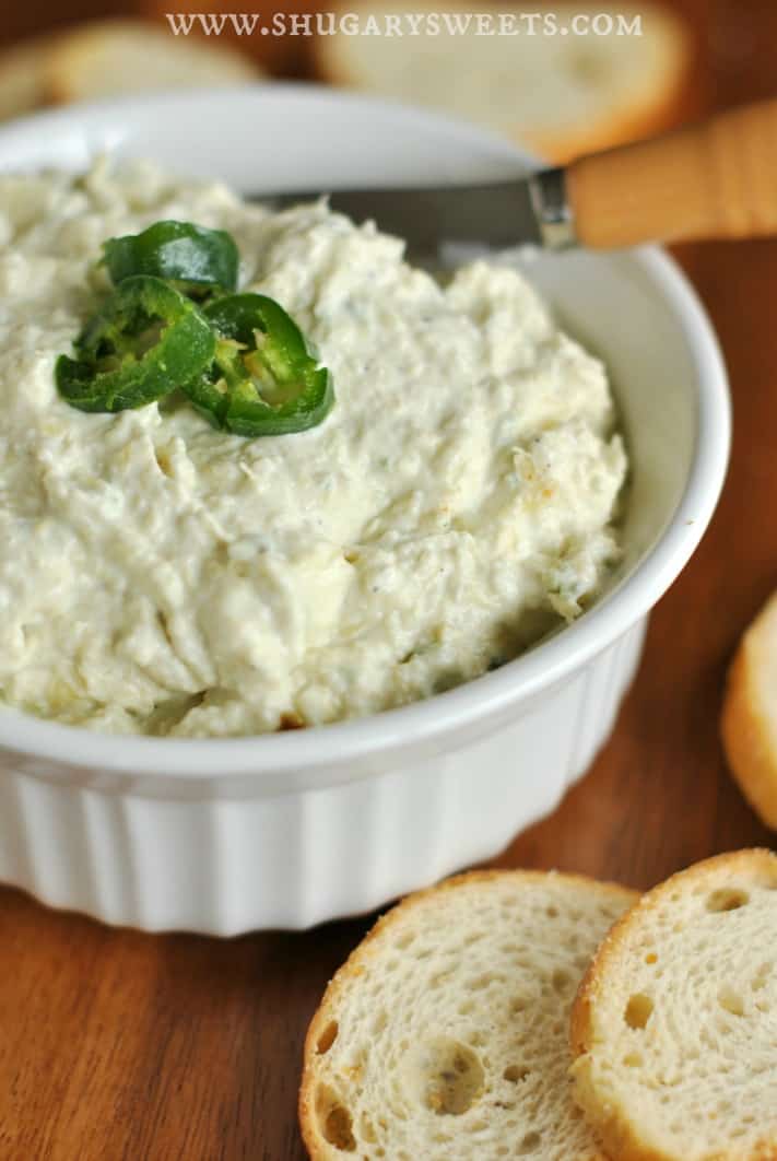 Spicy artichoke jalapeno dip in a white bowl topped with three slices of fresh jalapenos.