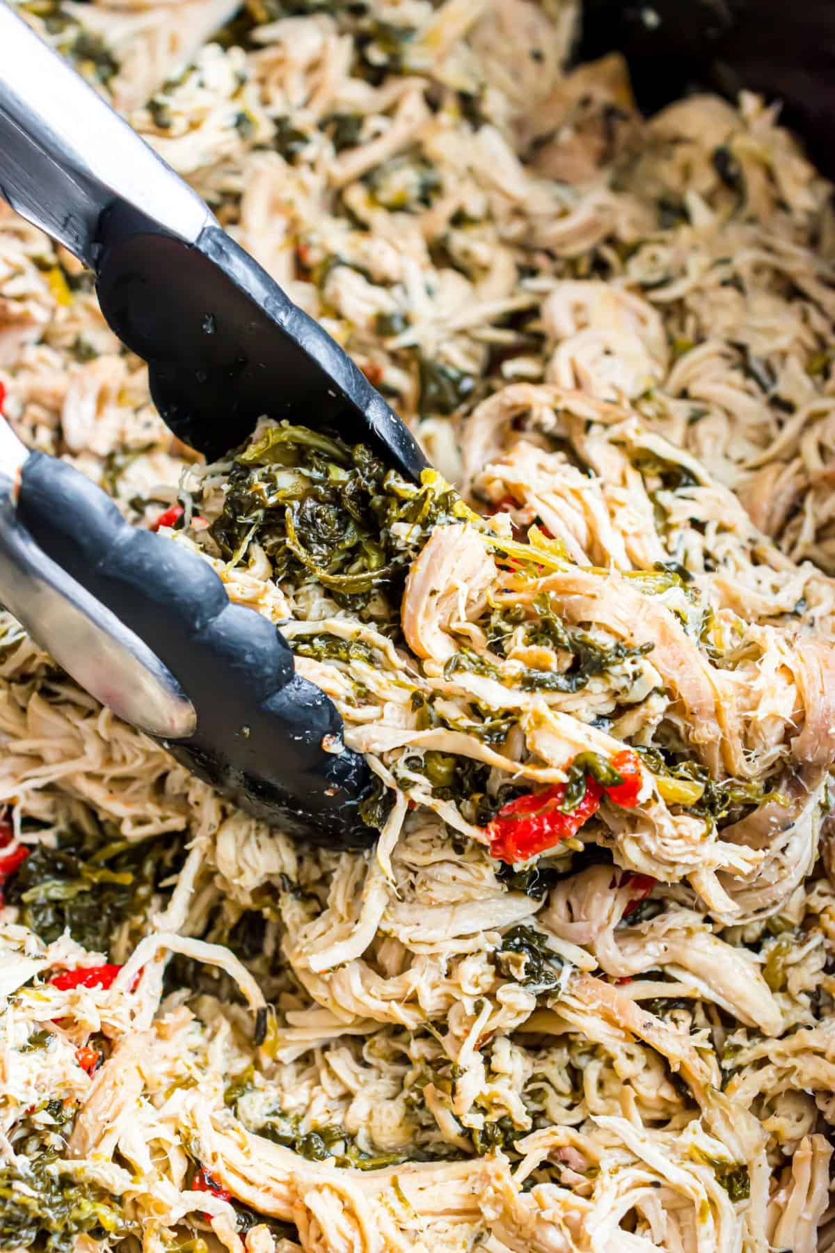 Shredded italian chicken in crockpot with tongs.