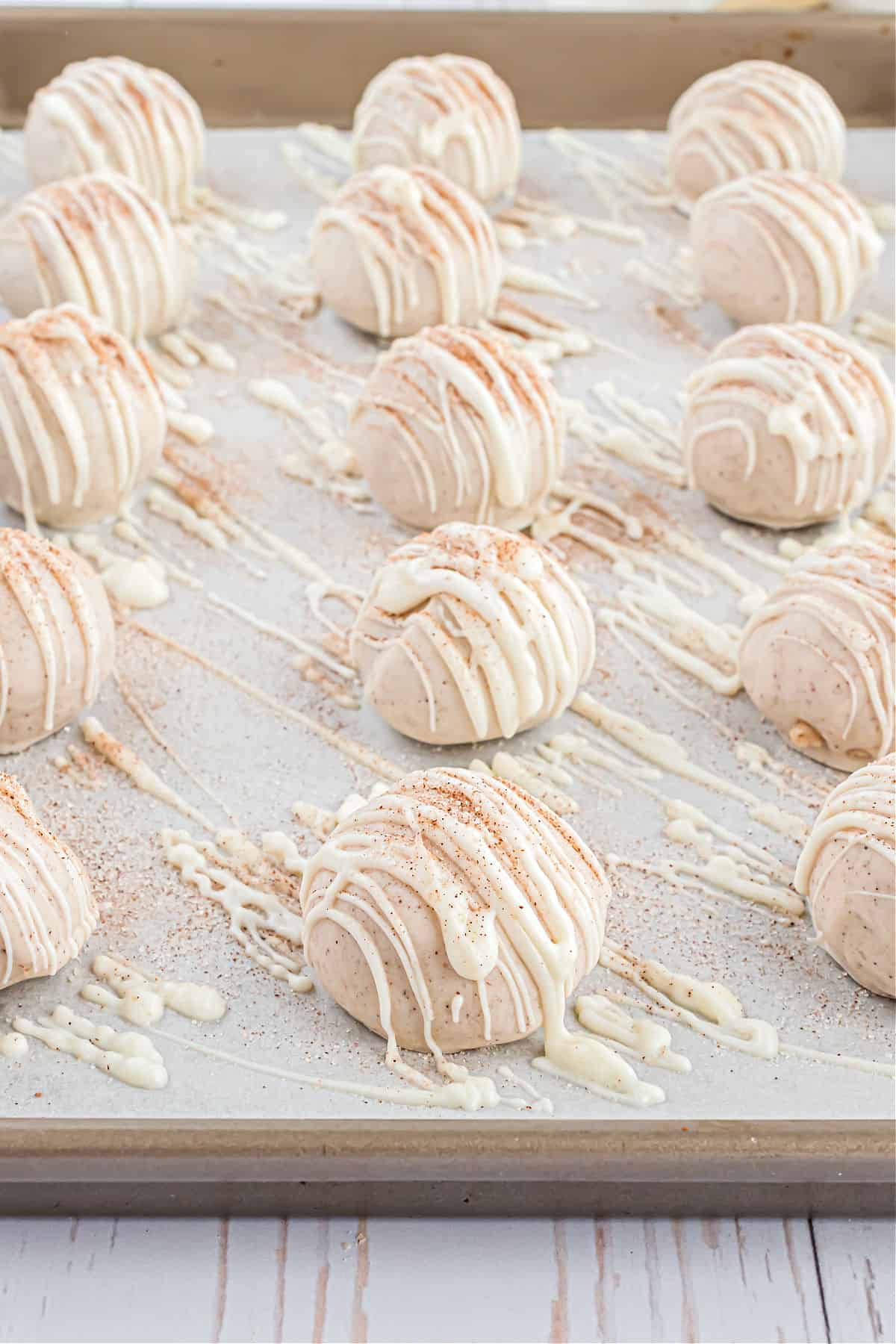 Cookie dough truffles dipped in white chocolate on a parchment paper lined cookie sheet.