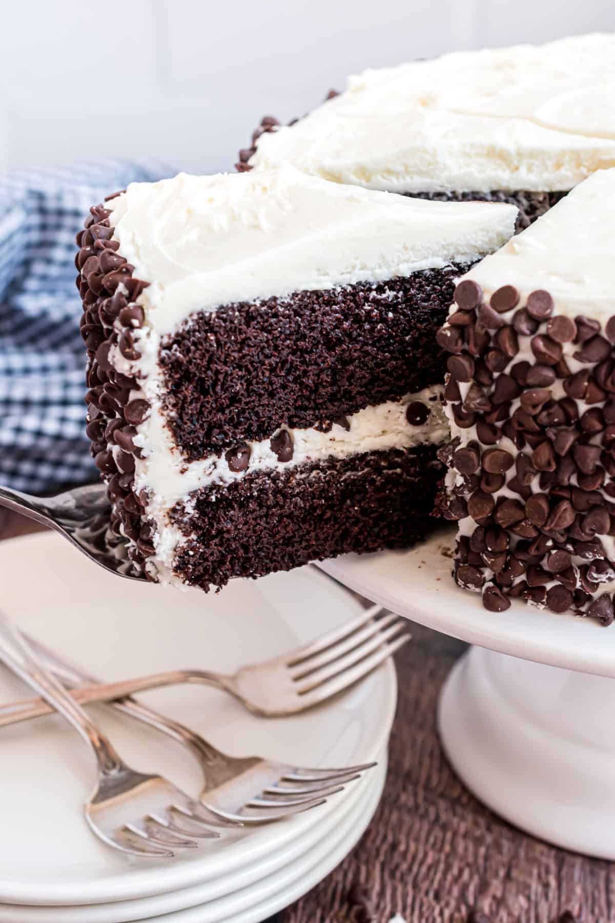 Vanilla frosted chocolate layer cake sliced and being removed from cake plate.